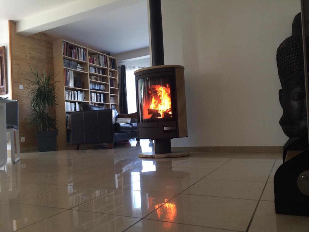 Installation d’un poêle à bois Stromboli N de la marque ROMOTOP, en pierre de grès, appareil flexible à 360°, offrant une large vision du feu.